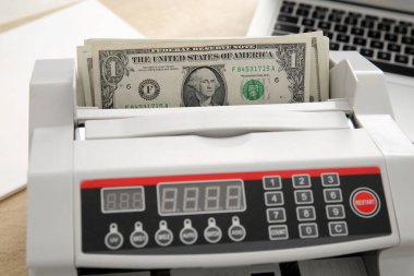 Cash counting machine with dollar banknotes on table in office, closeup