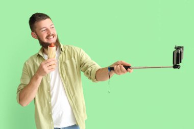 Lezzetli sosisli mutlu genç adamın portresi yeşil arka planda selfie çekiyor.