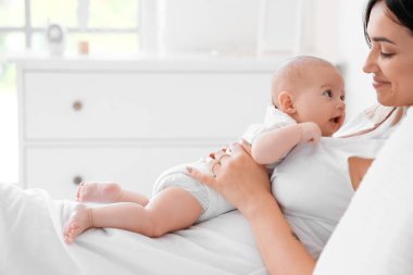 Mutlu bir anne ve küçük tatlı bir bebek evde yatakta yatıyor.