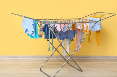 Sarı duvarın yanındaki kurutucuda asılı temiz bebek kıyafetleri.