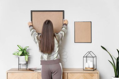 Evdeki duvarda boş bir çerçeve asılı genç bir kadın.