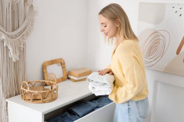 Katlanmış giysileri evdeki çekmeceye koyan genç bir kadın.