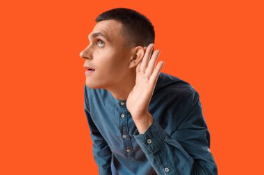 Turuncu arka planda işitme sorunu olan genç bir adam.