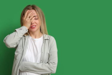 Yeşil arka planda facepalm yapan genç bir kadın.