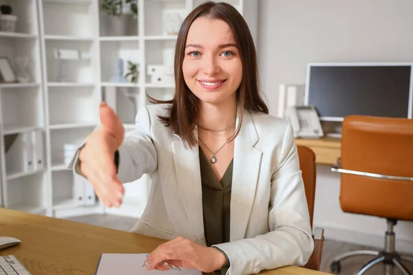 Young businesswoman reaching out for handshake at table in office