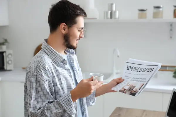 Young man with newspaper and coffee cup in kitchen