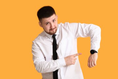 Sarı arka planda kol saatini gösteren genç iş adamı. Zaman yönetimi kavramı