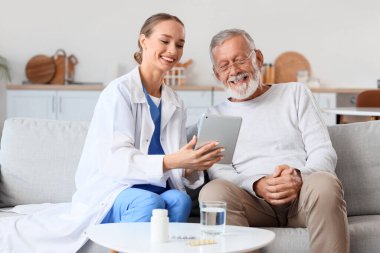 Evde tablet bilgisayar kullanan bakıcısı olan yaşlı bir adam.