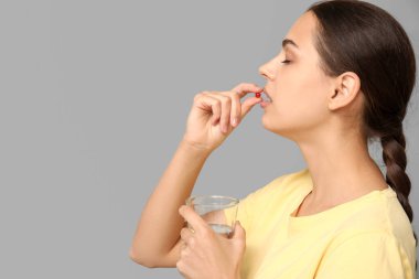 Gri arka planda A vitamini alan güzel genç bir kadın.