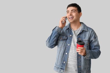 Elinde kahve fincanı olan mutlu genç adam arka planda cep telefonuyla konuşuyor.