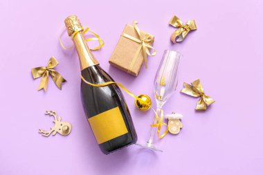 Cam kaplı bir şişe şampanya, Noel süslemeleri ve leylak arkaplanlı bir hediye kutusu.