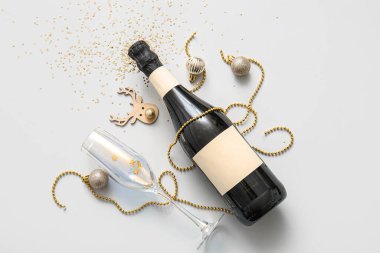 Cam kaplı bir şişe şampanya ve gri arka planda Noel süslemeleri.