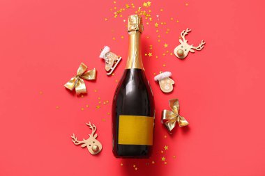 Noel süslemeleri ve kırmızı arka planda konfeti olan bir şişe şampanya.
