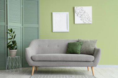 Gri kanepe, bitki ve katlanmış ekran ile şık bir oturma odası.