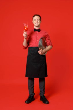 Kırmızı arka planda bir bardak kokteyl olan genç bir barmen.