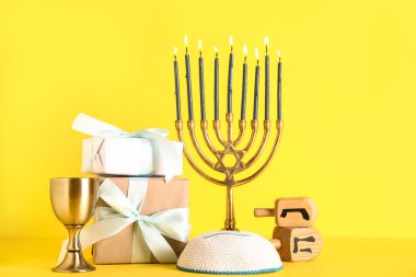 Hediye kutuları, fincanları ve sarı arka planda dreidleri olan Menorah. Hanuka kutlaması