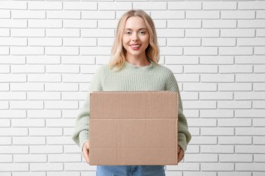 Açık karton kutulu, tuğla kaplamalı genç bir kadın.