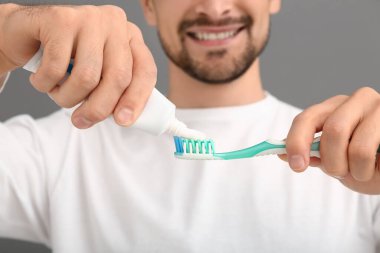 Gri arka planda diş macunu sıkan yakışıklı adam, yakın plan.