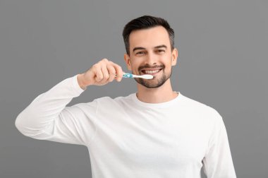 Gri arka planda dişlerini fırçalayan yakışıklı bir adam.