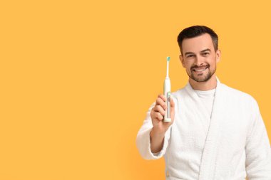 Sarı arka planda elektrikli diş fırçası olan yakışıklı bir adam.