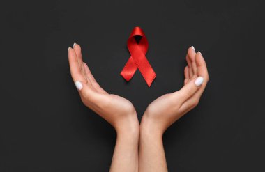 Siyah arka planda kırmızı kurdeleli bir kadın eli. AIDS Günü konsepti