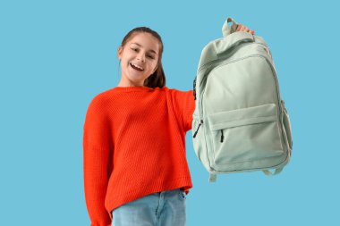 Mavi arka planda sırt çantası olan küçük okul kızı.