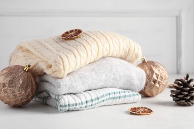 Süveter yığını, kurutulmuş limon, kozalak ve ışıklı arka planda Noel topları içeren kompozisyon, yakın plan