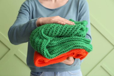 Yeşil arka planda farklı stil süveter yığını tutan kadın.