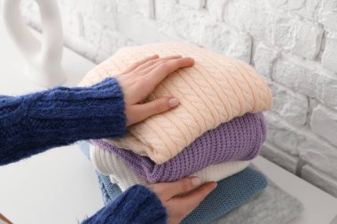 Odadaki tuğla duvarın yanındaki masada değişik stil süveter yığını olan kadın, yakın plan.