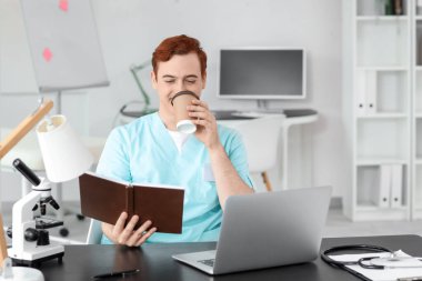 Erkek doktor klinikteki masada kahve içiyor.