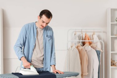 Çamaşır odasında çamaşır ütüleyen genç adam.