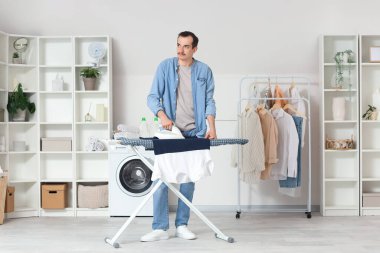 Çamaşır odasında çamaşır ütüleyen genç adam.