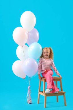 Güzel balonları ve mavi arka planda basamakları olan sevimli küçük bir kız.