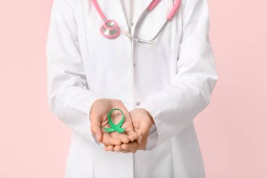 Pembe arka planda yeşil kurdeleli kadın doktor, yakın plan. Karaciğer kanseri farkındalığı