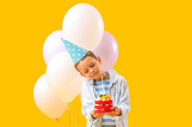 Doğumgünü pastası ve sarı arka planda balonları olan şirin bir çocuk.