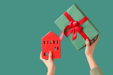 Noel hediyesini tutan eller ve yeşil arka planda kırmızı ev modeli