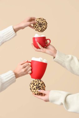 Şekerlemeli bardakları tutan eller ve bej arka planda kurabiyeler.