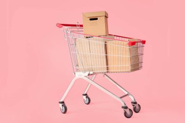 Pembe arka planda karton kutular olan alışveriş arabası.