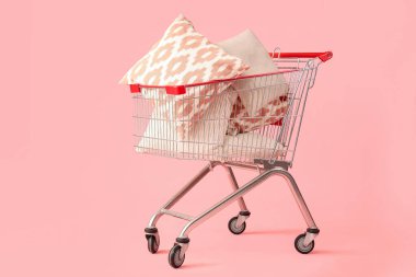Pembe arka planda yastıkları olan alışveriş arabası.