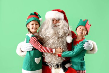 Küçük elfler yeşil arka planda Noel Baba 'ya sarılıyorlar.