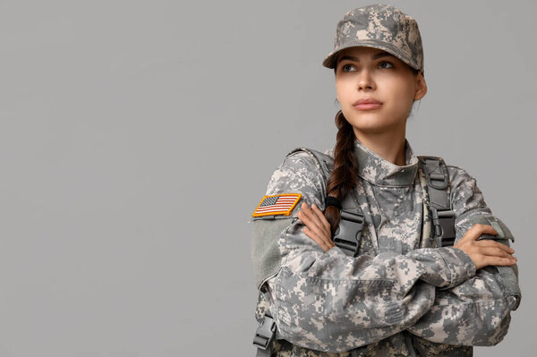 Confident young female soldier in uniform on grey background