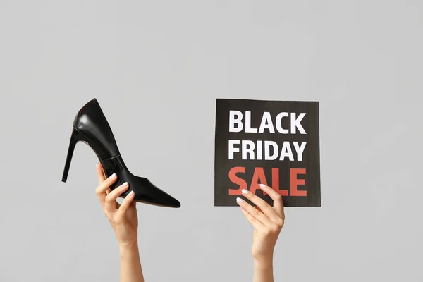 Female hands holding poster with text BLACK FRIDAY SALE and stylish shoes on grey background