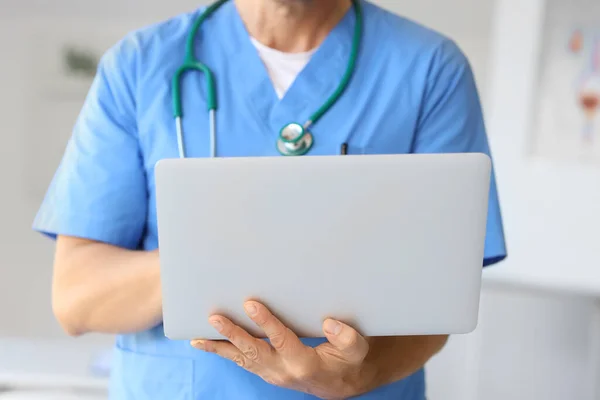 Mature doctor with laptop in medical office, closeup