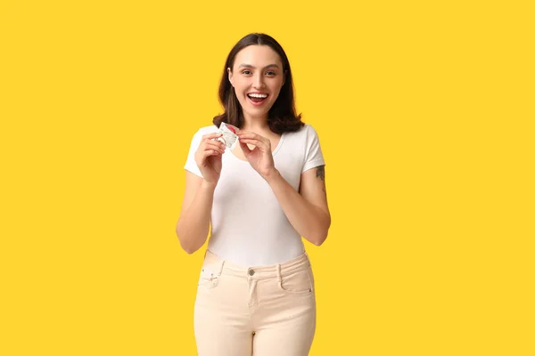 黄色の背景に開いたコンドームを持つ美しい若い女性 安全なセックスコンセプト — ストック写真