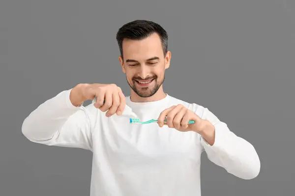 Schöner Mann Drückt Zahnpasta Auf Bürste Auf Grauem Hintergrund — Stockfoto