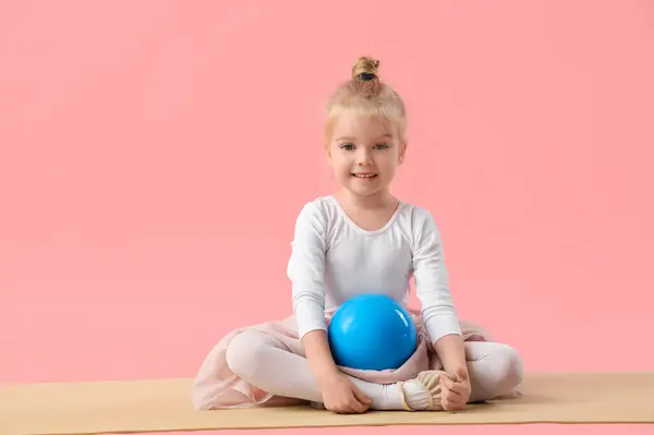 Cute little girl with gymnastic ball sitting on mat against pink background