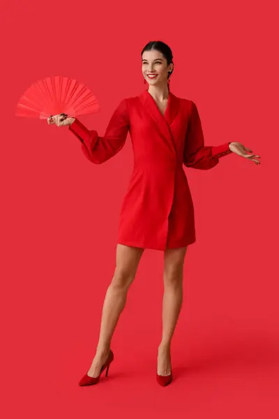 Beautiful young happy woman with fan on red background. Chinese New Year celebration