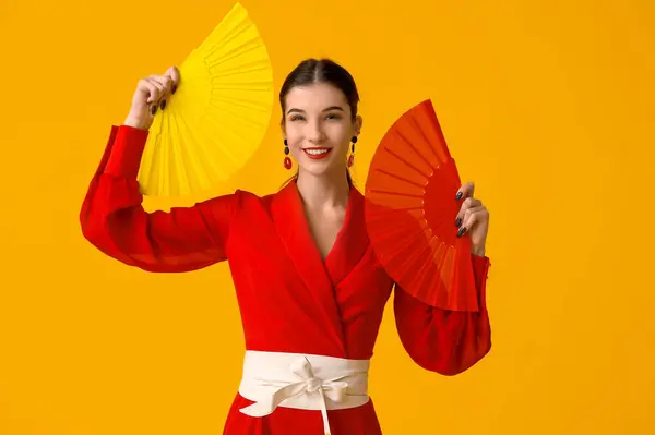 Beautiful young happy woman with fans on yellow background. Chinese New Year celebration