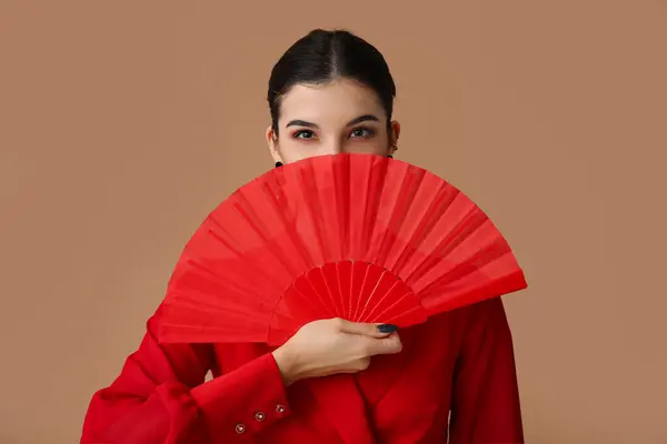 Beautiful young woman with fan on brown background. Chinese New Year celebration