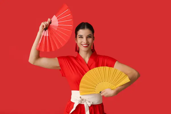 Beautiful young happy woman with fans on red background. Chinese New Year celebration